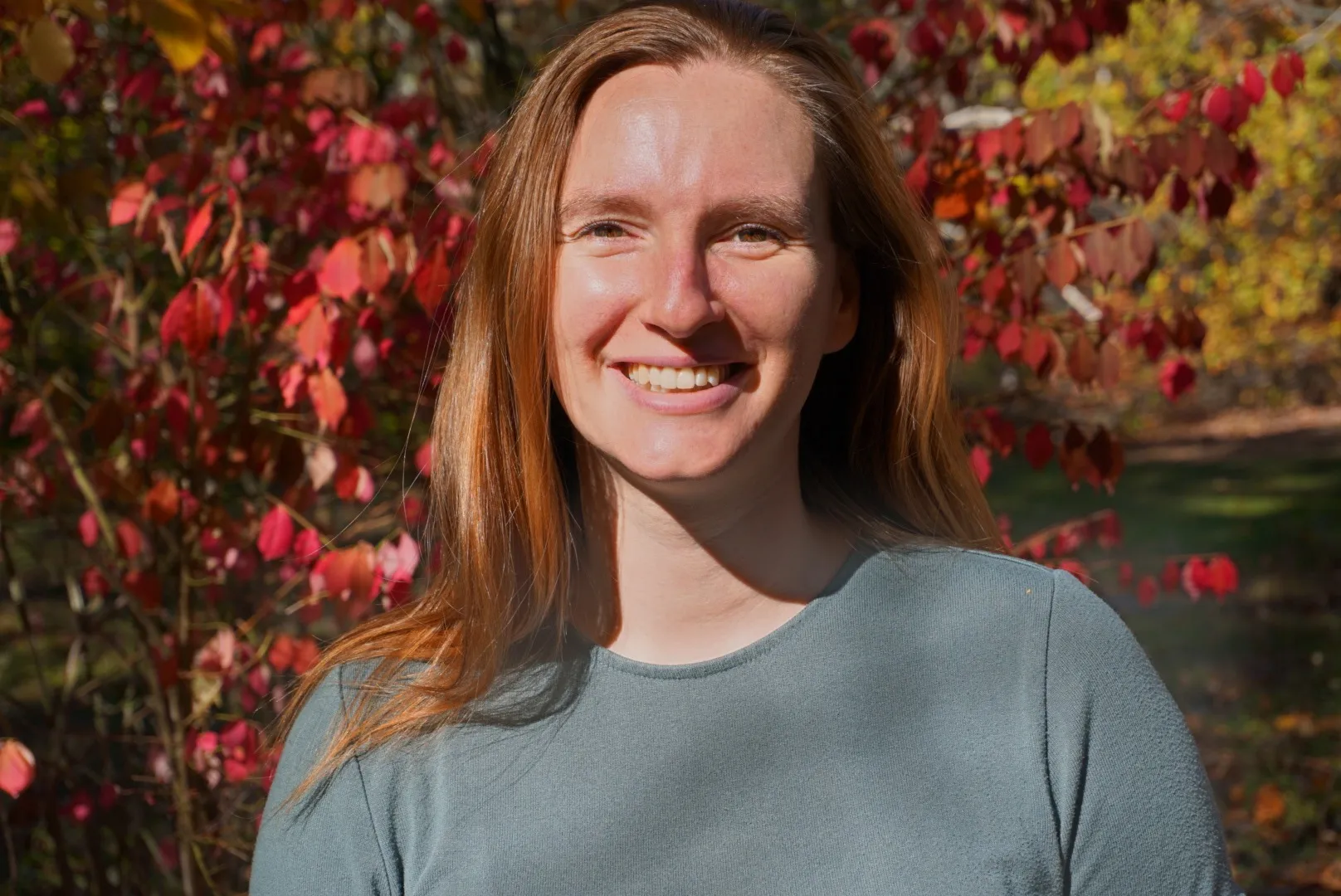 Madison Friend smiling outdoors in front of red fall leaves